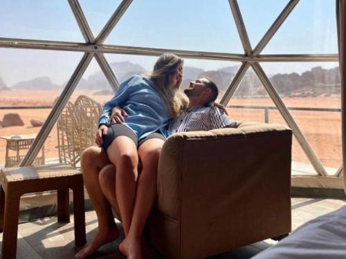 a man and woman sitting on a couch in front of a window at Karam Wadi Rum camp in Wadi Rum
