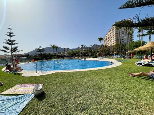 a large swimming pool with people sitting on the grass at El Coloso de SteraM Flats Benalmádena in Benalmádena