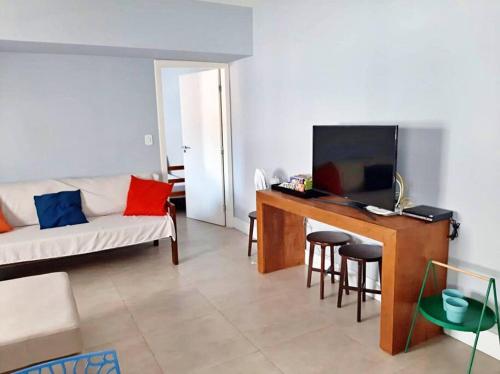 ein Wohnzimmer mit einem Sofa und einem Schreibtisch mit einem TV in der Unterkunft Apartamento charmoso no centro de Ubatuba in Ubatuba