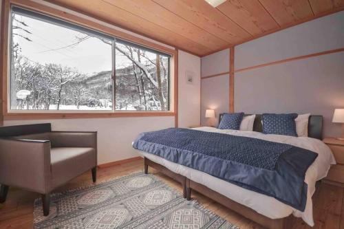 a bedroom with a bed and a window and a chair at Hakuba Colonsay- Amazing views 3bdr 2bth cottage in Hakuba