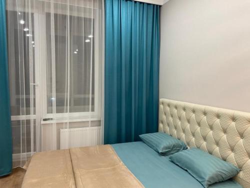 een slaapkamer met een bed met blauwe lakens en een raam bij Уютная квартира в центре столицы in Taldykolʼ