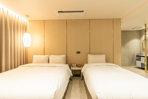 two beds in a hotel room with white sheets at Hotel The Grang Seogwipo in Seogwipo