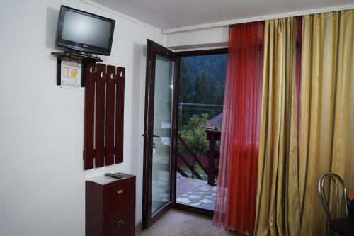 a room with a television and a door to a balcony at Passiflora in Voineasa