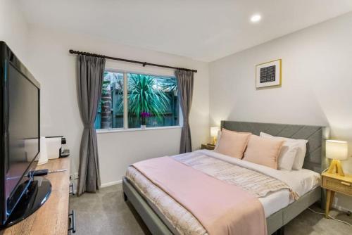 a bedroom with a bed and a tv and a window at Albany Bolthole with Queen Beds and Kitchenette in Auckland