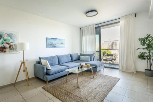 uma sala de estar com um sofá azul e uma mesa em Vibrant 2BR apt w Balcony 5-min from the Beach by Sea N' Rent em Tel Aviv