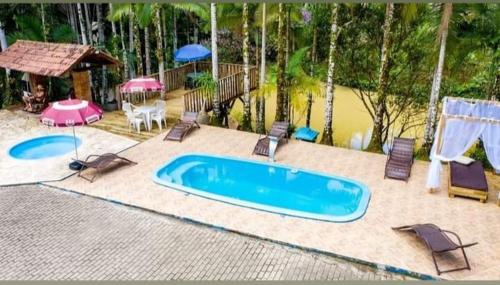 una piscina en un patio trasero con sillas y sombrillas en Suíte alvenaria casal., en Guabiruba