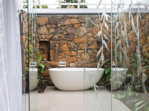 a bathroom with a bath tub in front of a stone wall at Buhwi Bira Byron Bay - Studio in Byron Bay