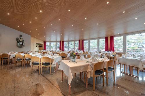 un comedor con mesas, sillas y cortinas rojas en Hotel Alex Business & SPA, en Naters