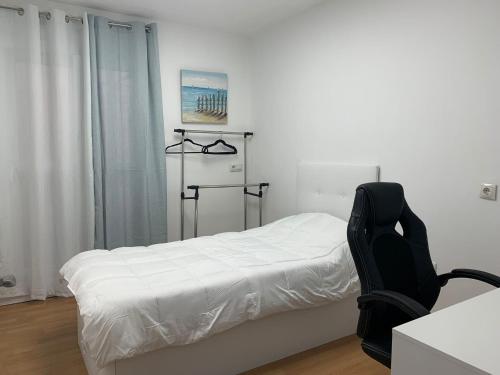 a bedroom with a white bed and a black chair at Apartamento Center Playa Almerimar in Almerimar