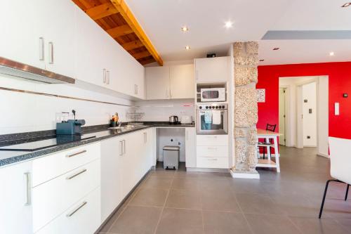a kitchen with white cabinets and a red accent wall at Casa dos Mouros - 2 Quartos e Cozinha - Serra da Estrela - Loriga in Loriga
