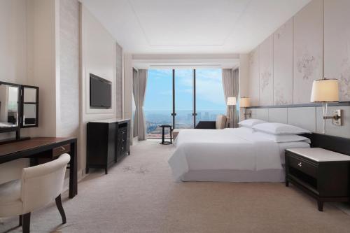 een slaapkamer met een bed, een bureau en een televisie bij Sheraton Qingdao Licang Hotel in Qingdao