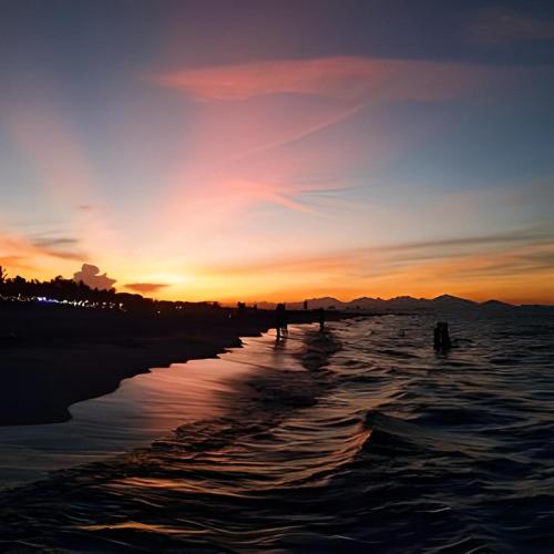 a sunset on the beach with people walking in the water at Cua Dai Beach Homestay in Hoi An