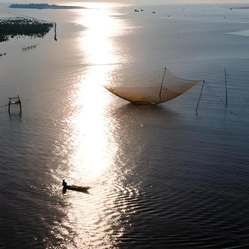 a man in the water with a boat in the water at Cua Dai Beach Homestay in Hoi An