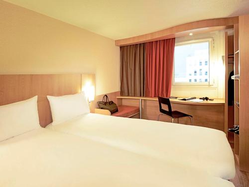 a hotel room with a large white bed and a desk at Ibis Évry-Courcouronnes in Evry-Courcouronnes