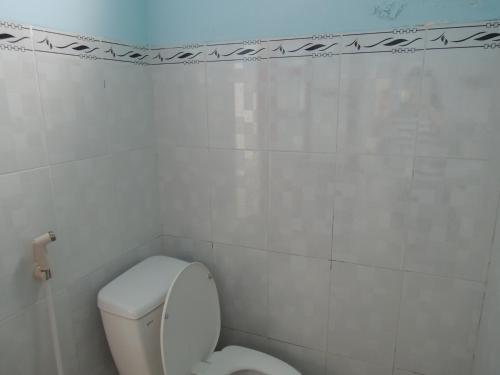 a bathroom with a toilet and a white tiled wall at Lang Chai Guesthouse in Mui Ne