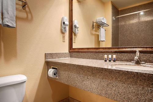 a bathroom with a sink and a toilet and a mirror at Days Inn & Suites by Wyndham Sam Houston Tollway in Houston