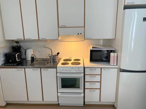 een keuken met witte kasten, een fornuis en een magnetron bij Kotimaailma - Kodikas kaksio saunalla Matinkylässä in Espoo