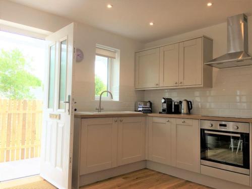 a kitchen with white cabinets and a sink and a window at Chy Bownder Cottage in Lostwithiel