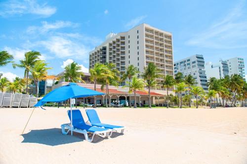 a blue umbrella and chairs on a beach with buildings at Courtyard by Marriott Isla Verde Beach Resort in San Juan