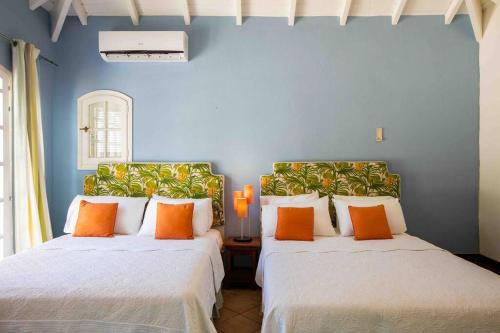 two beds in a room with blue walls and orange pillows at Villa La Josephine, Terre Basses in Baie Longue