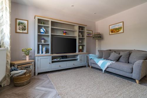 un salon avec un canapé gris et une télévision dans l'établissement Fleming Cottage - Contemporary Cotswold Home, 
