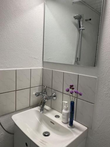 a bathroom sink with a mirror and a vase of flowers at Ferielejlighed til 2 personer in Ebeltoft