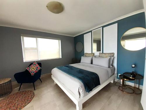 een slaapkamer met een bed en een stoel en 2 ramen bij 201 Coral Island, 88 Coral Road, Bloubergstrand in Bloubergstrand