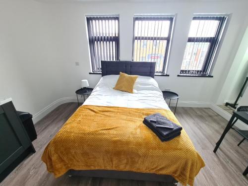 1 Schlafzimmer mit einem Bett mit gelber Decke und 2 Fenstern in der Unterkunft Homestay by BIC Legends 3 in Batley Carr