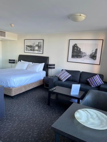 シドニーにあるPrestige Hyde Park Studio Apartmentのベッドとソファ付きのホテルルーム
