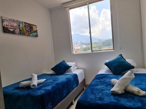 een slaapkamer met 2 bedden met blauwe lakens en een raam bij Apartamento lujoso en Medellín in Sabaneta