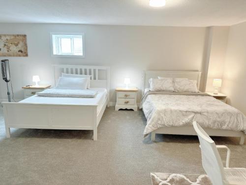 a white bedroom with two beds and two tables at Beautiful entire basement with Netflix in Stittsville