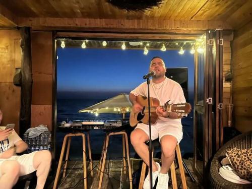 Um homem sentado num bar a tocar guitarra. em Hotel Prana Beach em Barú