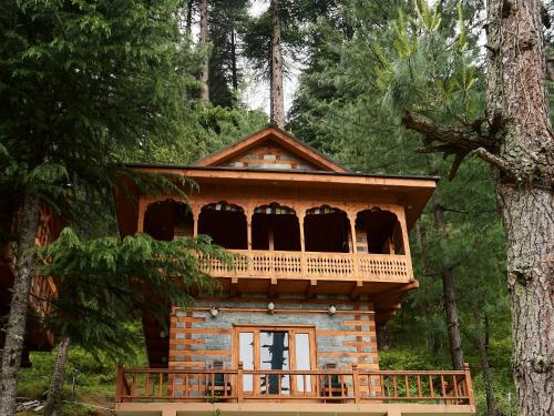 a log cabin with a balcony in the woods at The Lazy and Slow in Nagar