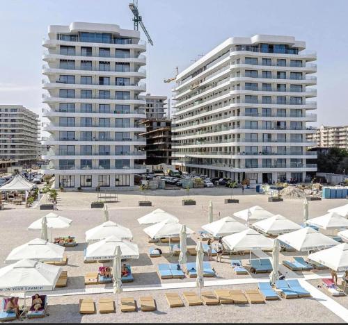 - une plage avec des parasols blancs, des chaises et des bâtiments dans l'établissement Black Sea Booking, à Mamaia