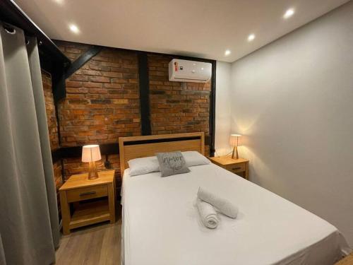 a bedroom with a white bed and a brick wall at Casa Enxaimel 02 em Pomerode in Pomerode