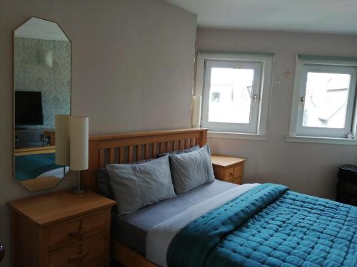 een slaapkamer met een bed met een blauwe deken en 2 ramen bij Aigas in Glasgow