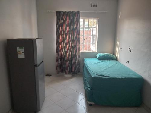 Habitación pequeña con cama y nevera. en Las Palmas Day & Night Guest House, en Pretoria