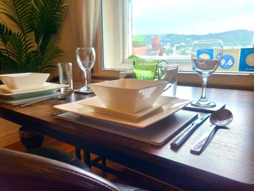 uma mesa de madeira com uma taça, pratos e copos de vinho em VALE VIEW APARTMENT, Prestatyn, North Wales - a smart and stylish, dog-friendly holiday let just a 5 min walk to beach & town! em Prestatyn