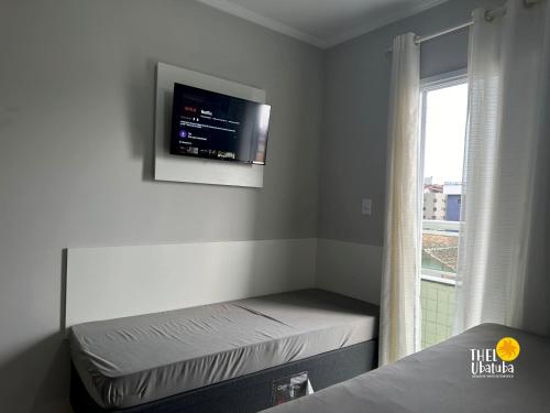 Zimmer mit einem Bett und einem TV an der Wand in der Unterkunft Conforto, 2 vagas garag lazer a poucos passos do mar! Apto 306/B, Ana Luiza - Praia Grande in Ubatuba