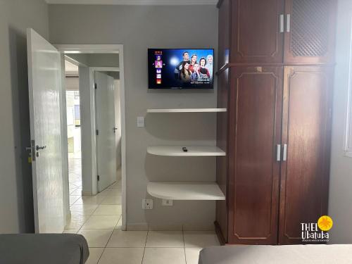 ein Wohnzimmer mit einem Fernseher an der Wand in der Unterkunft Conforto, 2 vagas garag lazer a poucos passos do mar! Apto 306/B, Ana Luiza - Praia Grande in Ubatuba