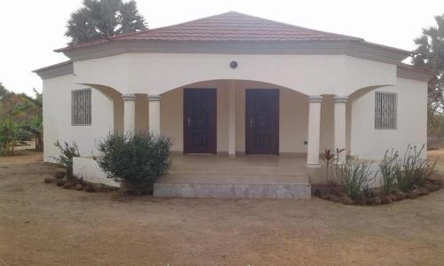 a small white house with brown doors and pillars at Carl and Veronica Guest House in Sanyang