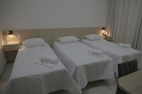 2 bedden in een hotelkamer met witte lakens bij Hotel San Gennaro in Santa Fé do Sul