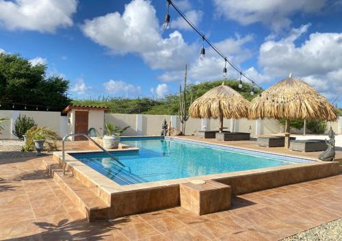 a swimming pool with benches and umbrellas at Pura Vida Aruba appartement Cama in Noord