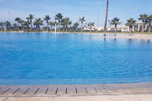 una gran piscina con palmeras en el fondo en appartement chic et ensoleillé ola blanca 2, en Dar Hamida