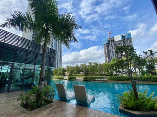 einen Pool mit zwei weißen Stühlen und einer Palme in der Unterkunft Greenfield Residence, Bandar Sunway by The Comfort Zone in Petaling Jaya