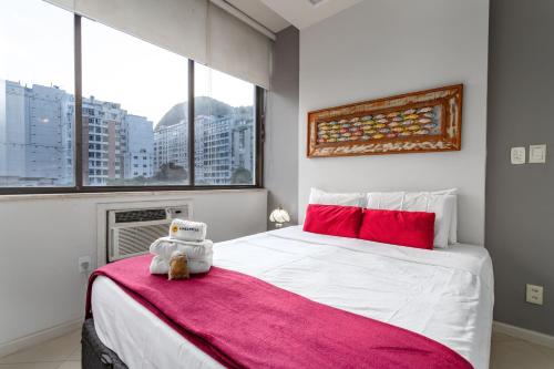 Un dormitorio con una gran cama blanca con almohadas rojas y un osito de peluche en Aconchego em Copacabana - 150m da praia - PI401 Z5, en Río de Janeiro