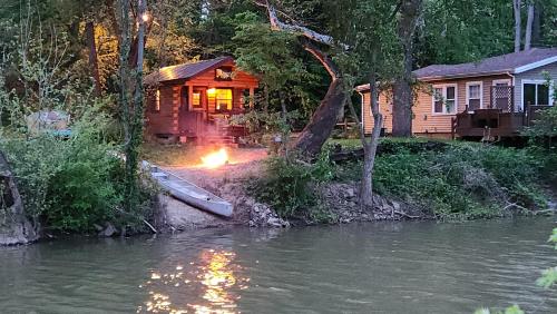 eine Hütte am Fluss mit einem Feuer davor in der Unterkunft River Log Cabins in Waterville