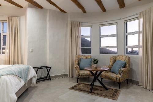 a bedroom with two chairs and a table and windows at Capri Sands Luxury Guest House in Capri Village