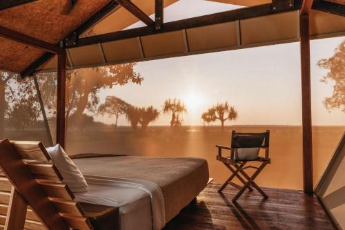 a room with a bed and a chair in a field at Bamurru Plains in Point Stuart