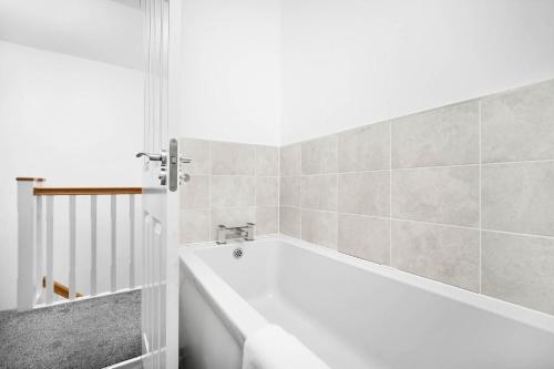 a white bath tub in a bathroom with tiles at Luxury 4 Bed House with En-suite, Games room, BBQ, On-site parking By Azura Nights in Birmingham